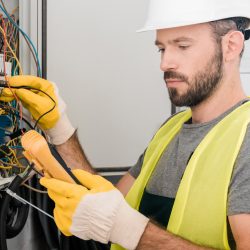 handsome electrician checking electrical panel with multimetr in corridor